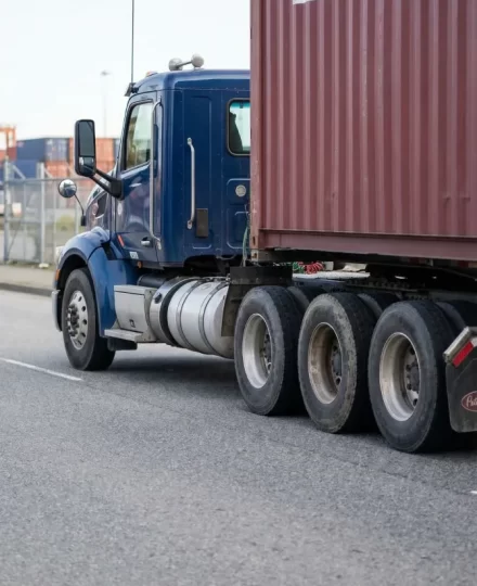 A highly detailed profile shot of a clean, robust, dark blue day-cab tractor unit under a heavily loaded 40-foot high-cube ocean container